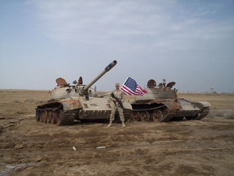 A soldier and an American flag beside two disabled tanks in the Iraqi desert, from the Lawless family album.