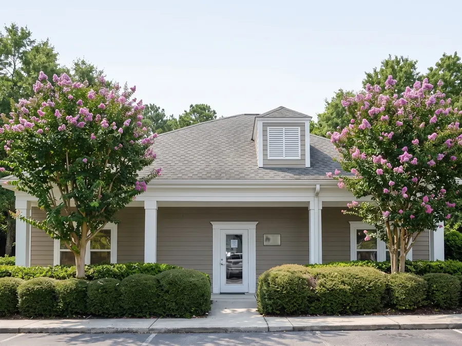 The Sun City Bluffton office at 16 William Pope Drive, Suite 104, behind crape myrtles and clipped hedges.