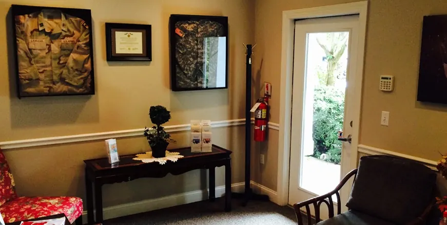 Inside Hilton Head Dental: a side table, framed Army uniforms and a certificate on the wall, and the door out to the garden.